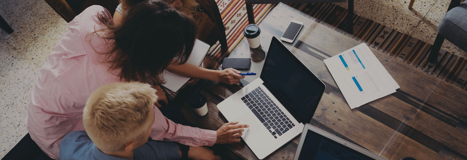 Photo of three people gathered around a table looking at a laptop