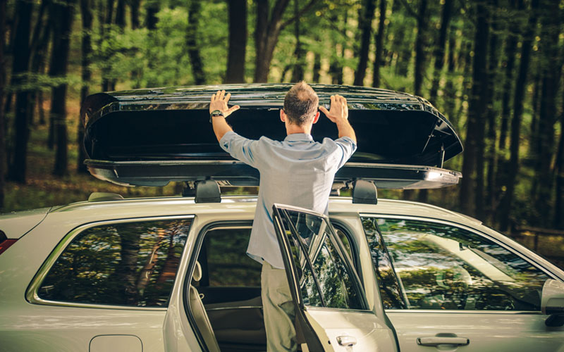 A photo of a man opening a storage container on top of his car