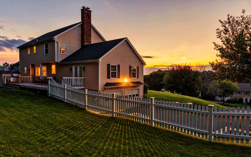 A photo of a beautiful home, white picket fence, and yard at sunset