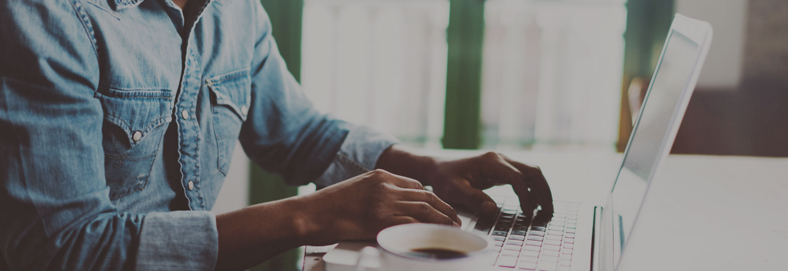 Photo of a man typing on a laptop with a cup of coffee