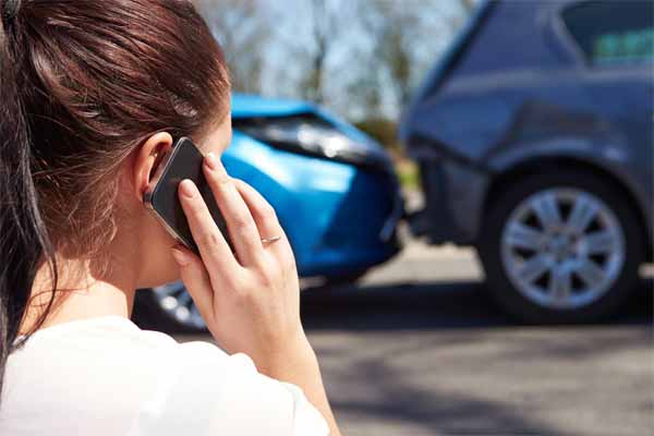 A young woman standing near a car collision talking on the phone