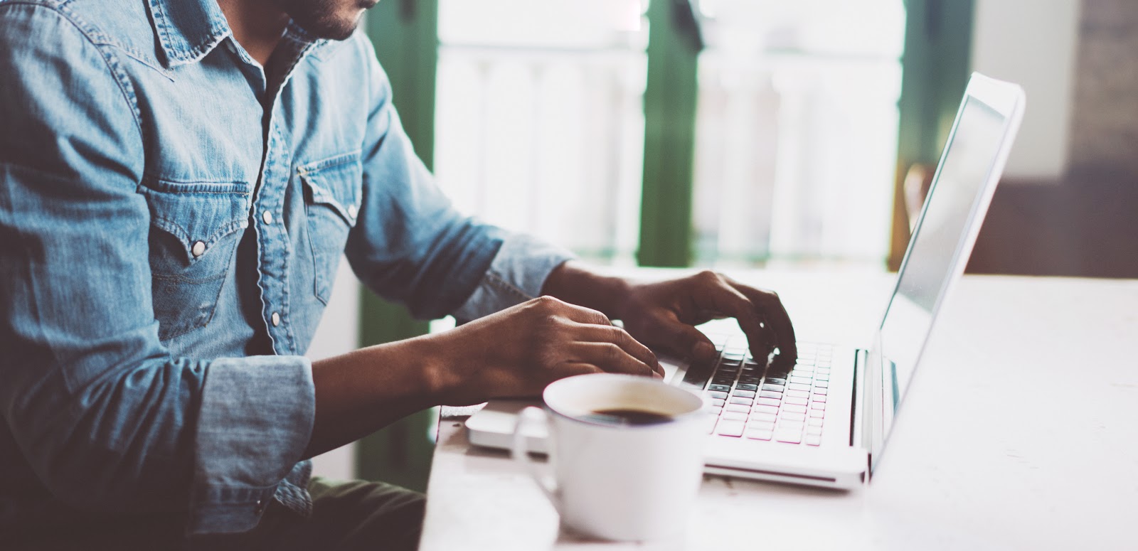 Photo of man typing on a laptop and drinking coffee