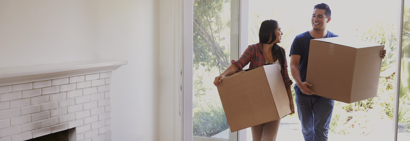 A man and woman walking into a home holding boxes